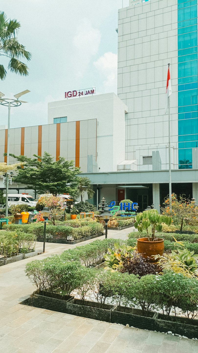 Modern hospital building with landscaped gardens and waiting emergency vehicles.