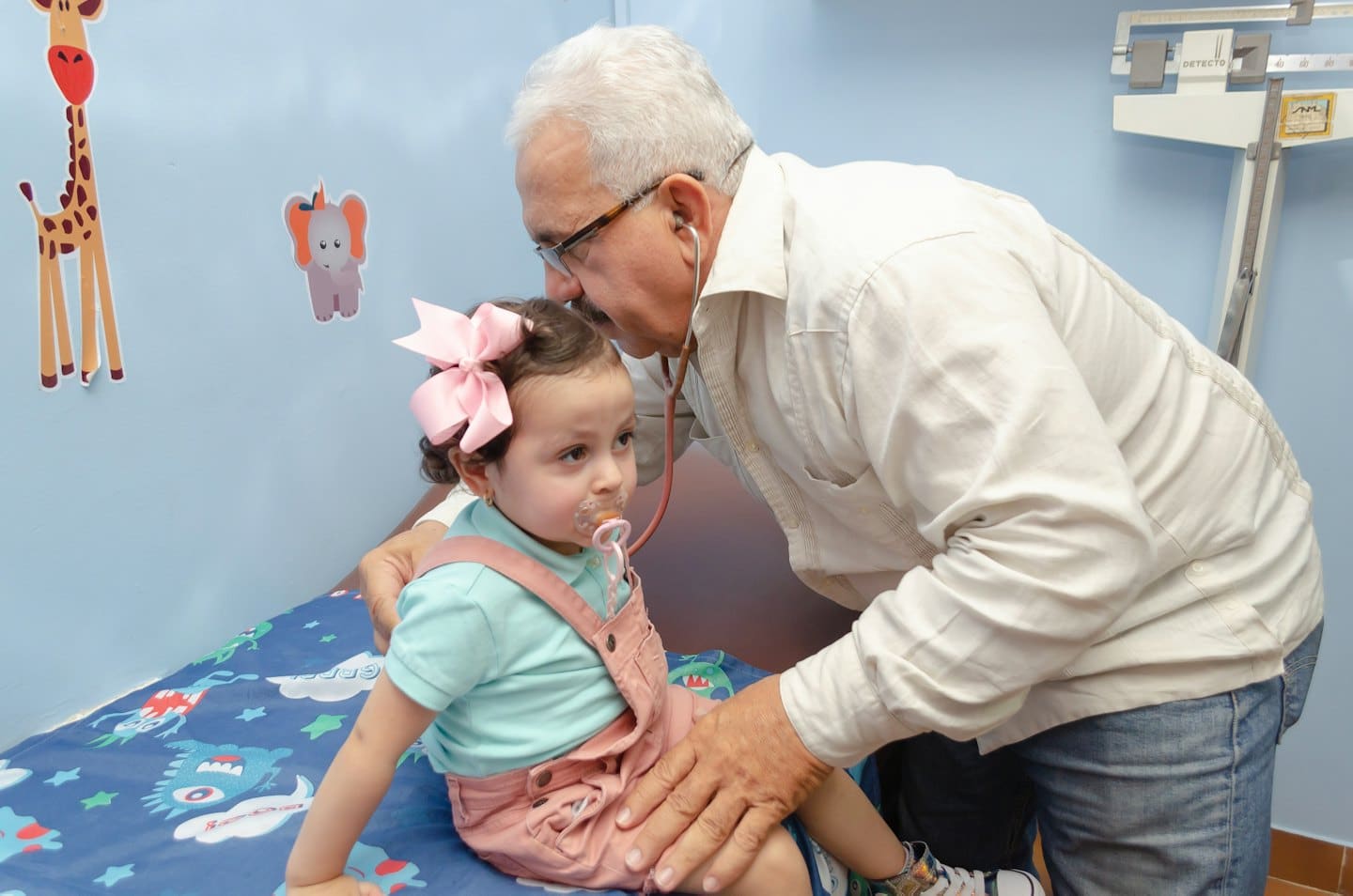 Pediatrician examines a young child sitting on an exam table.